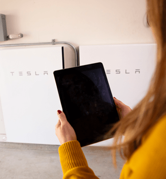 woman looking at tablet in front of Tesla batteries